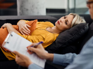 Thoughtful woman lying down on psychiatrist's couch during an ap