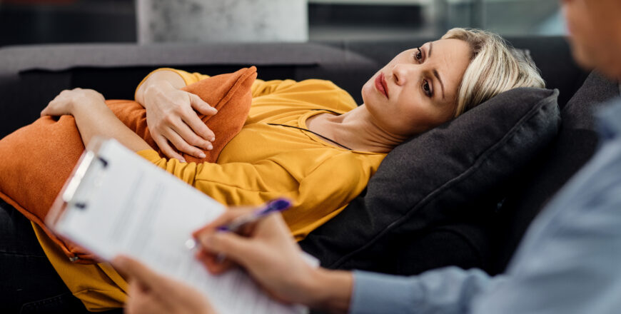 Thoughtful woman lying down on psychiatrist's couch during an ap